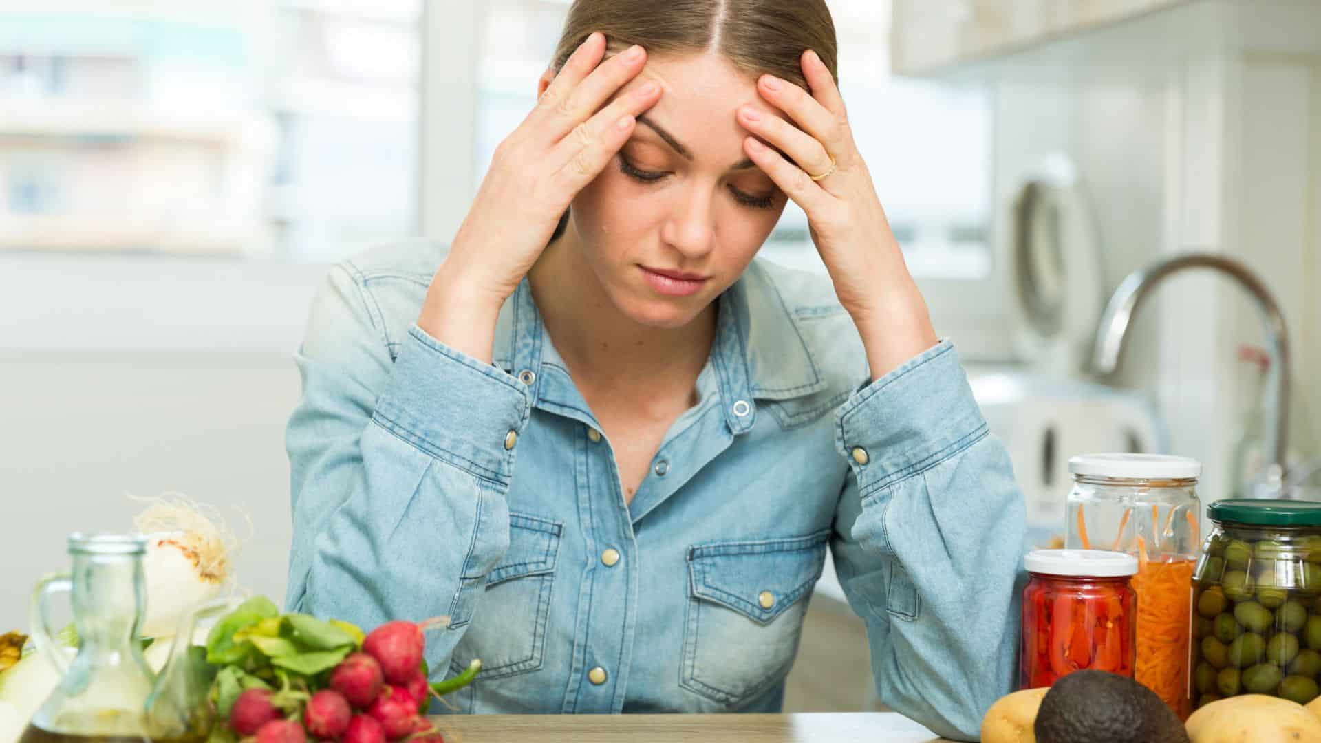 Frustrated woman with head in hands surrounded by food on kitchen counter.