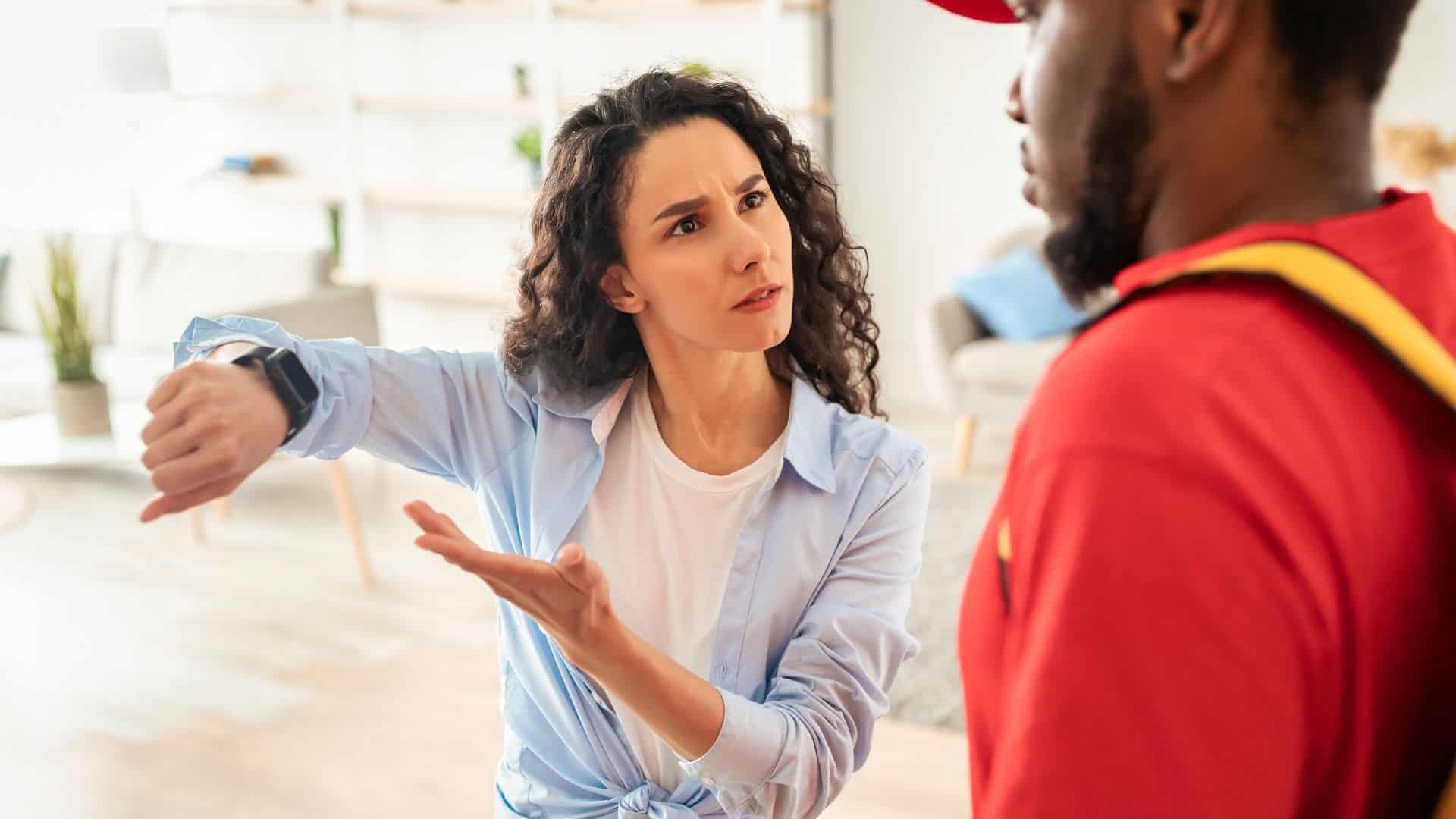 Frustrated female customer pointing at watch, delivery man is late