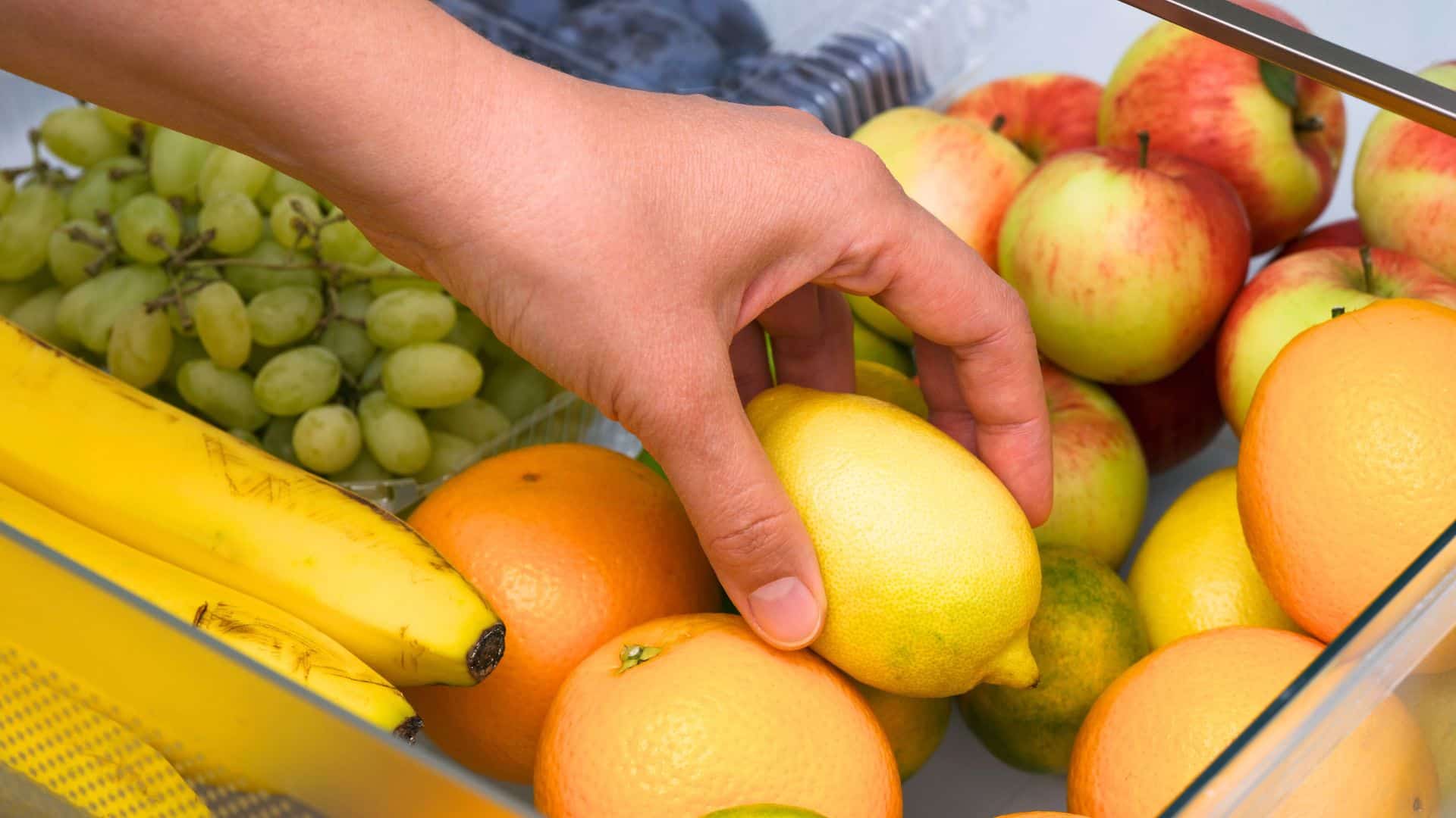 Woman getting a lemon from fridge drawer full of fruits